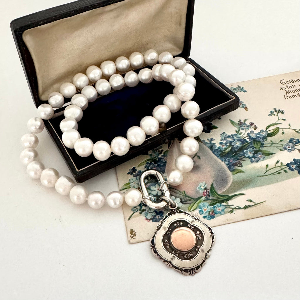 Image of Vonk Jewellery pearl and antique watch fob necklace on a vintage postcard and vintage jewellery box