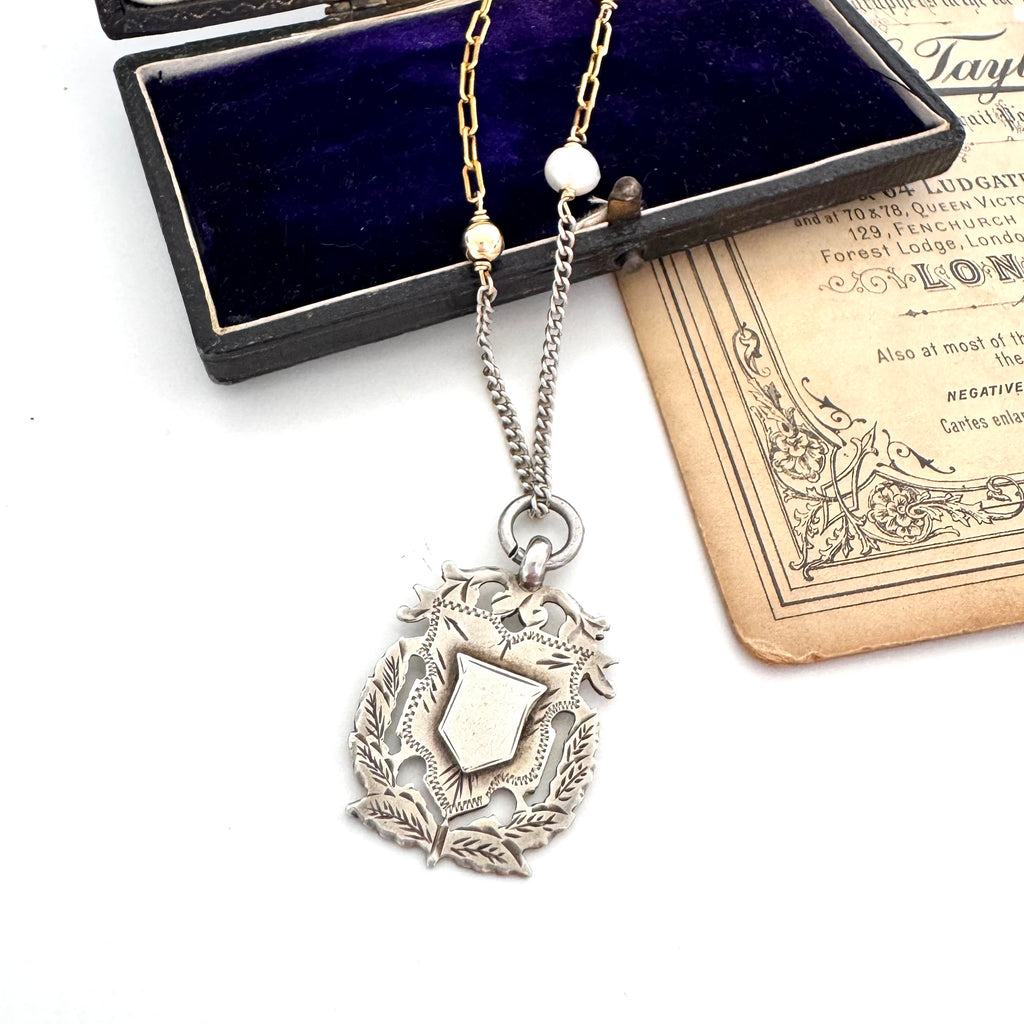 Antique 1898 watch fob necklace on a white background and with an old postcard and jewellery box