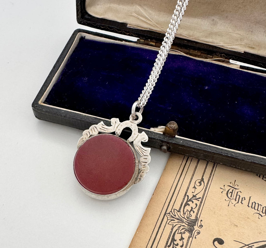 Antique 1905 watch fob necklace with a carnelian stone in a silver setting on an open book