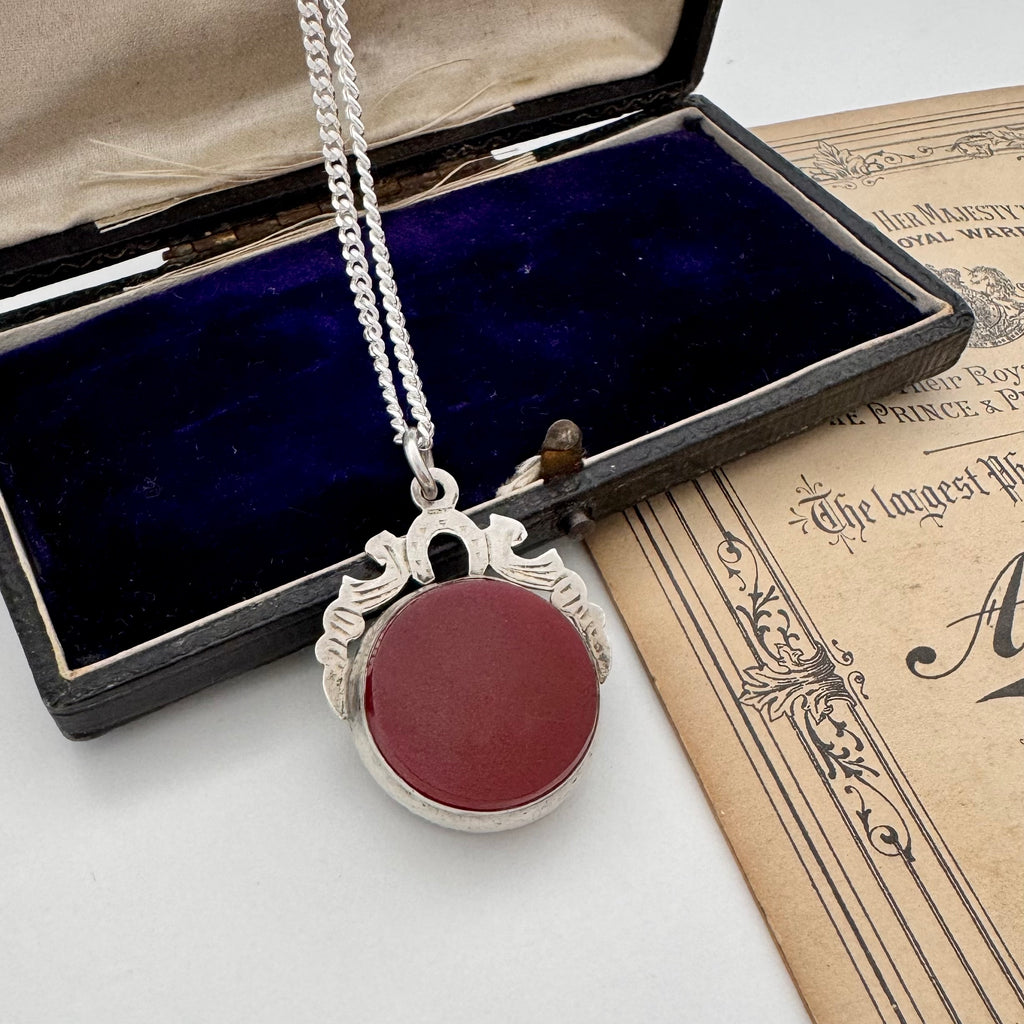 Silver 1905 watch fob necklace with a carnelian stone in an open jewelry box on an old document.