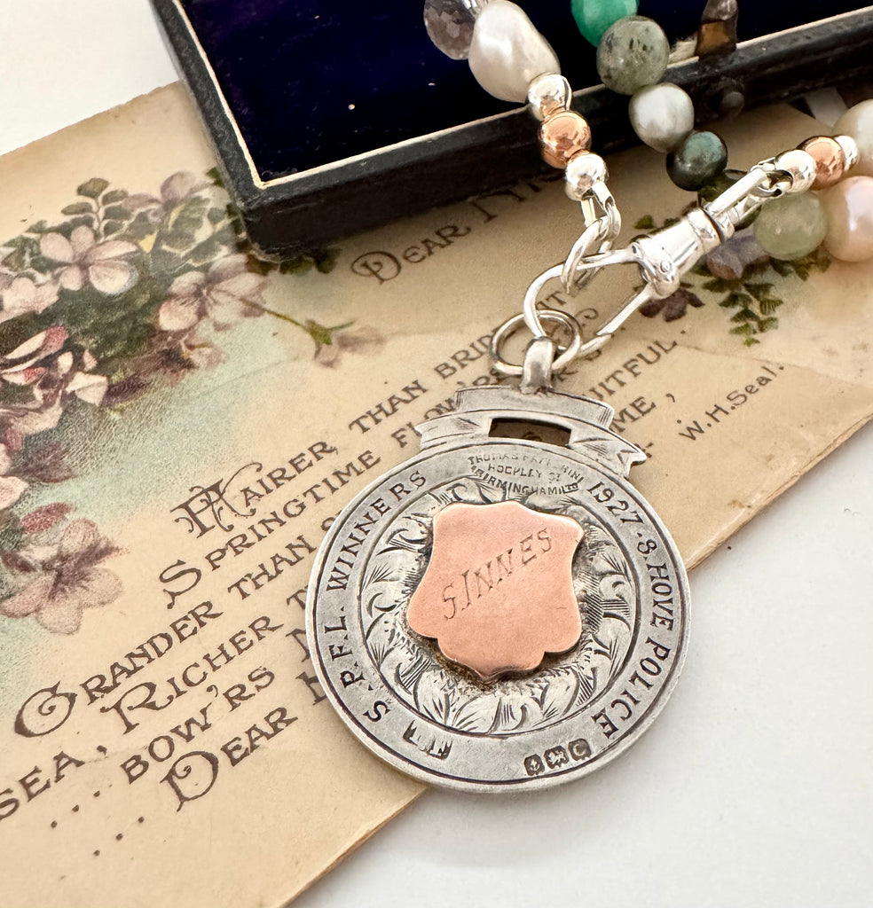 Vonk Jewellery 1927 watch fob and pearl, crystal and gemstone necklace on a vintage jewellery box and vintage postcards.