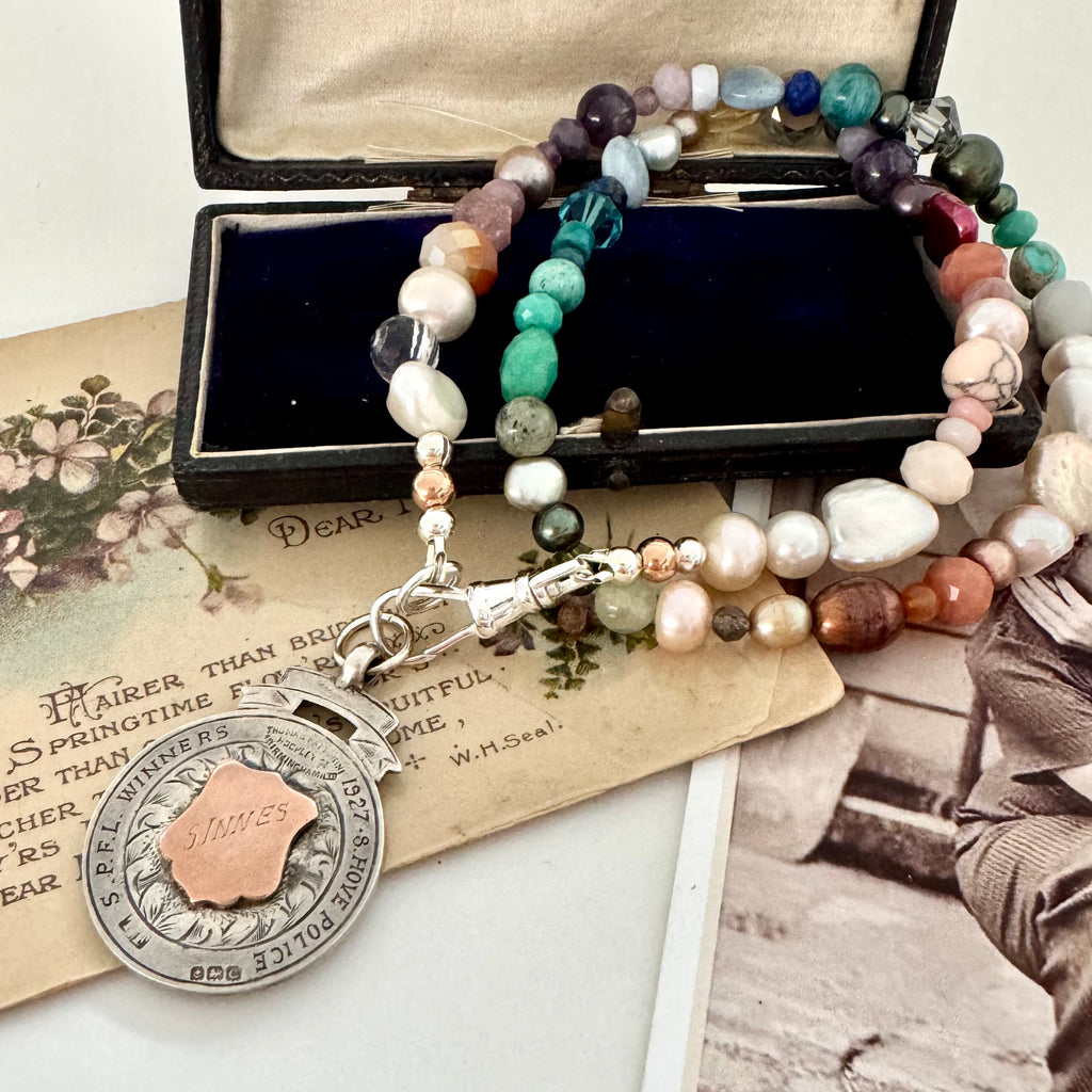 Vonk Jewellery 1927 watch fob and pearl, crystal and gemstone necklace on a vintage jewellery box and vintage postcards.