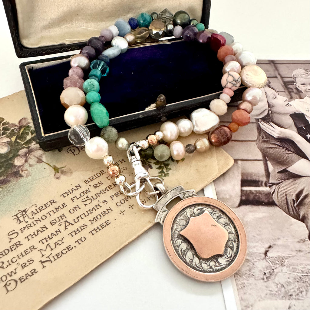 Vonk Jewellery 1927 watch fob and pearl, crystal and gemstone necklace on a vintage jewellery box and vintage postcards.