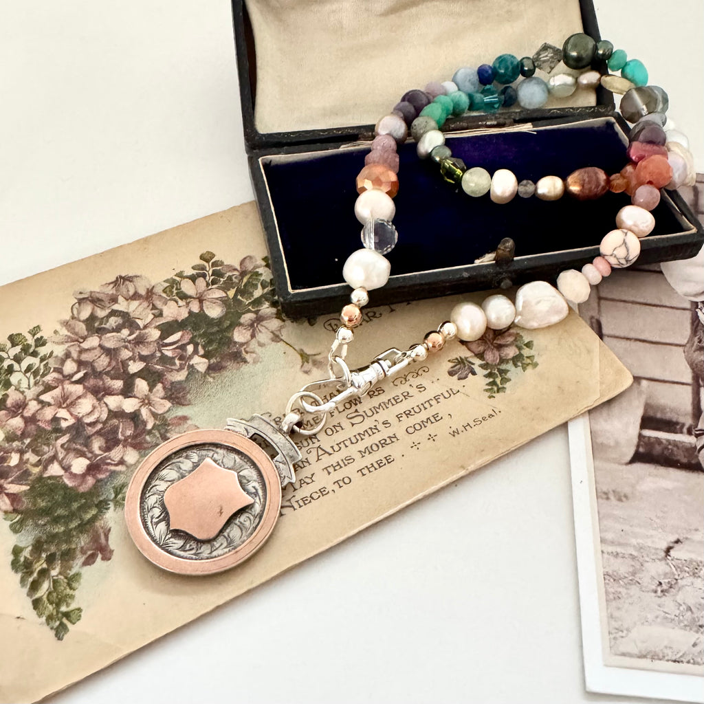 Vonk Jewellery 1927 watch fob and pearl, crystal and gemstone necklace on a vintage jewellery box and vintage postcards.