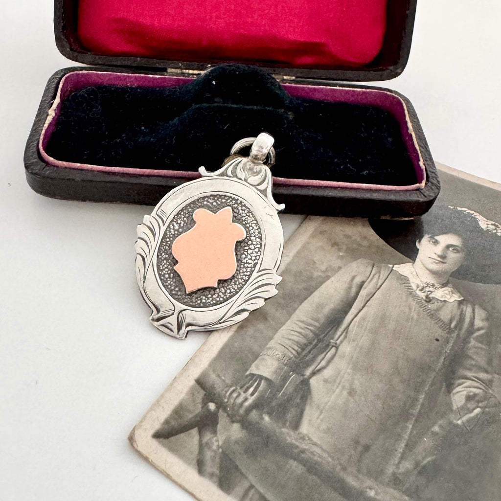 Silver and rose gold 1933 watch fob pendant in an open velvet box with an old photograph of a woman.