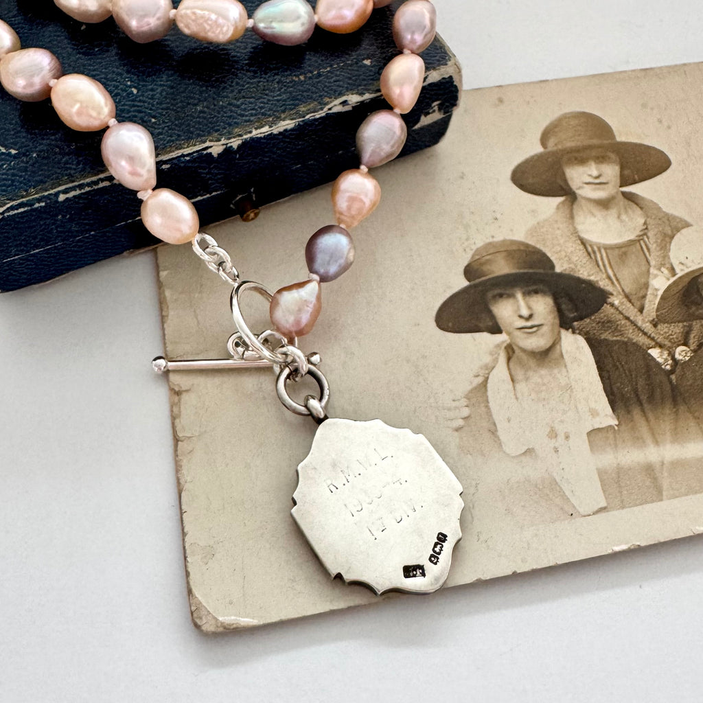 Pearl necklace and 1933 watch fob with a silver clasp on an old photograph of women wearing hats.