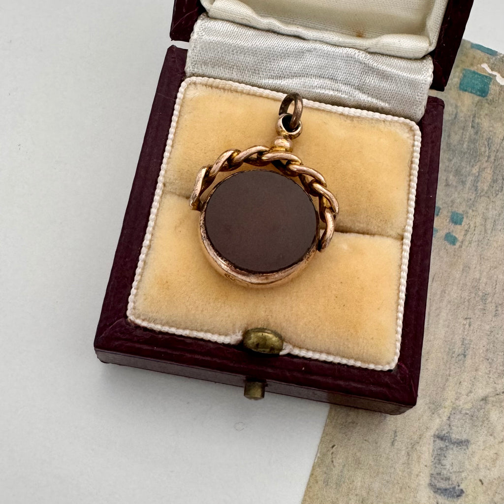 9ct rose gold antique swivel fob with a dark stone in a jewelry box on a textured surface