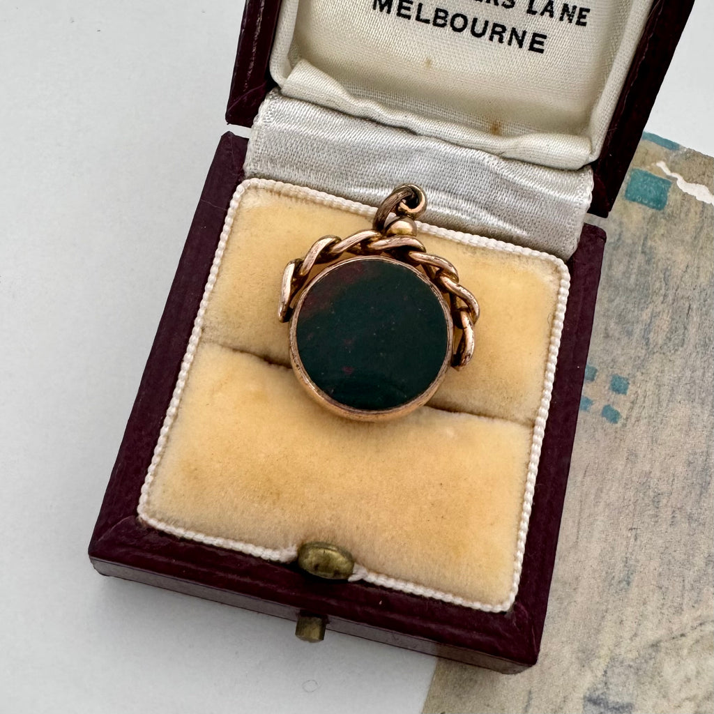 9ct rose gold antique swivel fob with a dark stone in a jewelry box on a textured surface