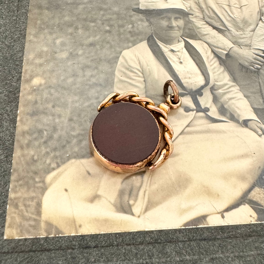 9ct rose gold antique swivel fob with a dark stone on an antique photo of an old woman