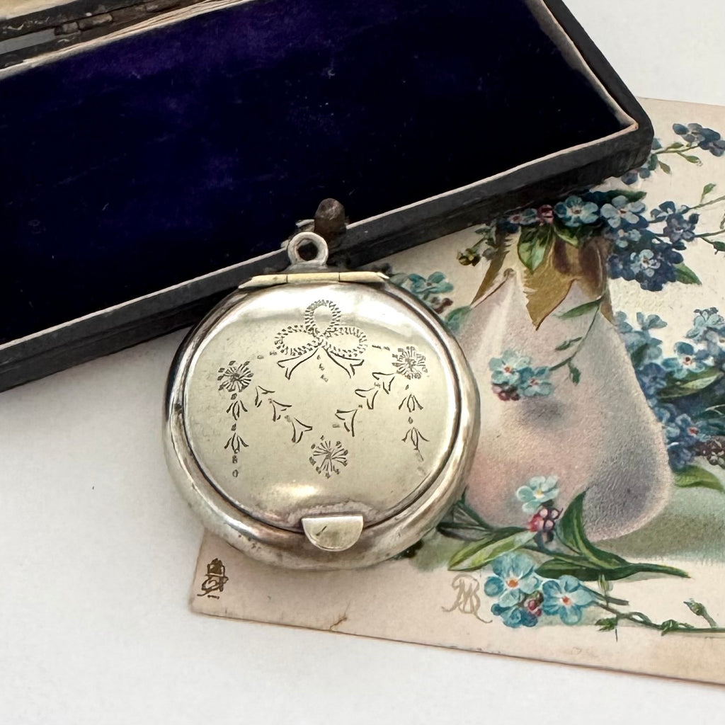 Silver compact mirror with floral engraving on a floral-patterned card