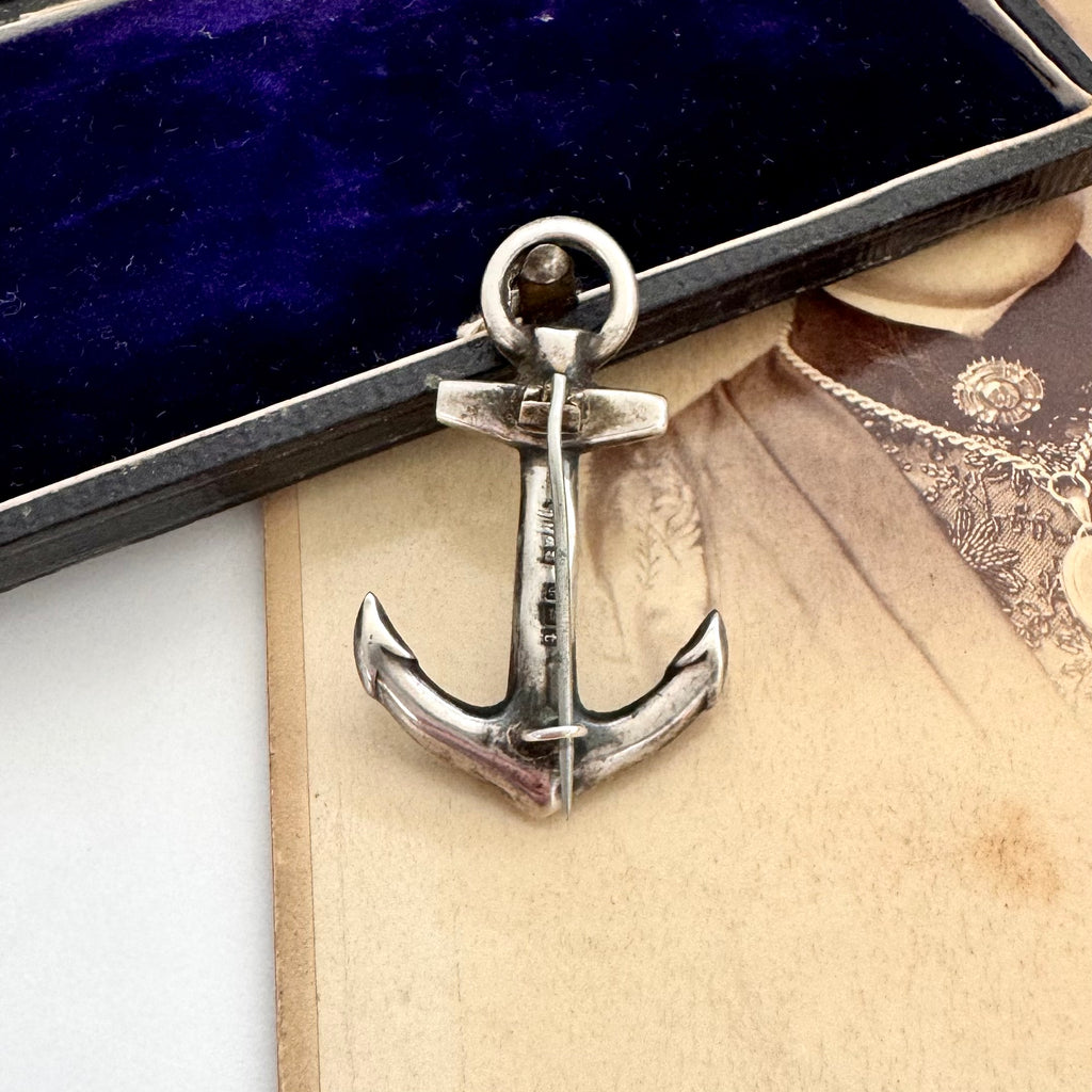 Silver anchor pendant on a textured surface with a dark blue box in the background