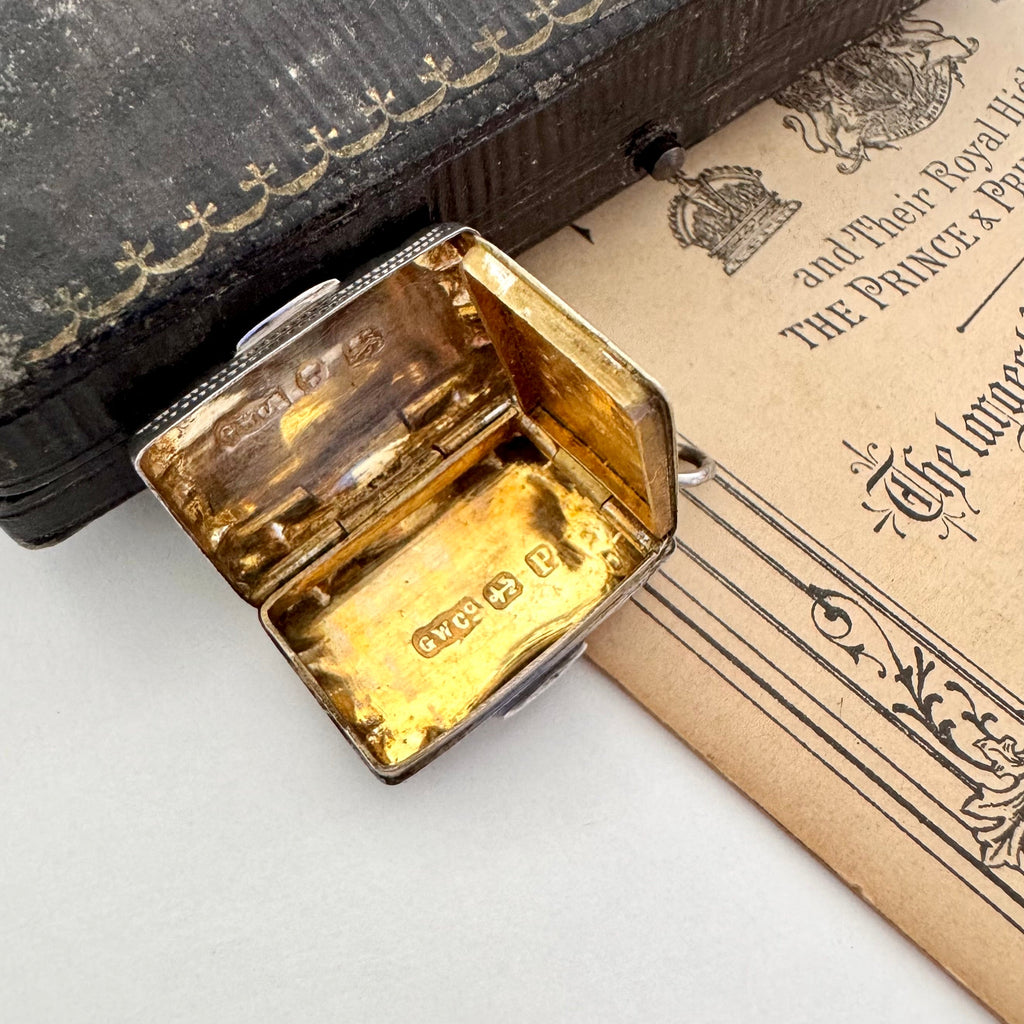 Antique 1864 sterling silver vinaigrette on an antique advertising material for a photography studio and a vintage jewellery box. The vinaigrette is open showing the grill inside.