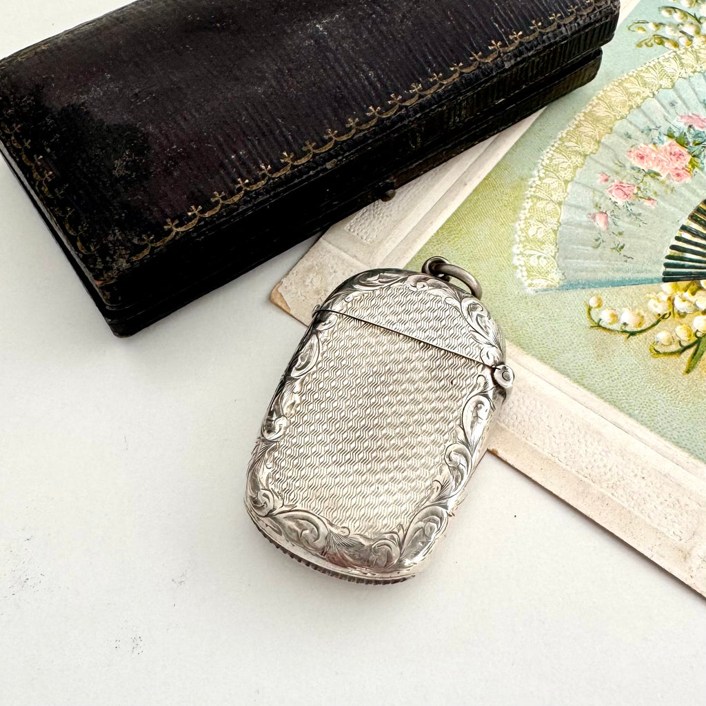 Antique 1879 Victorian silver vesta case on a white background with a vintage postcard and old box in the background.