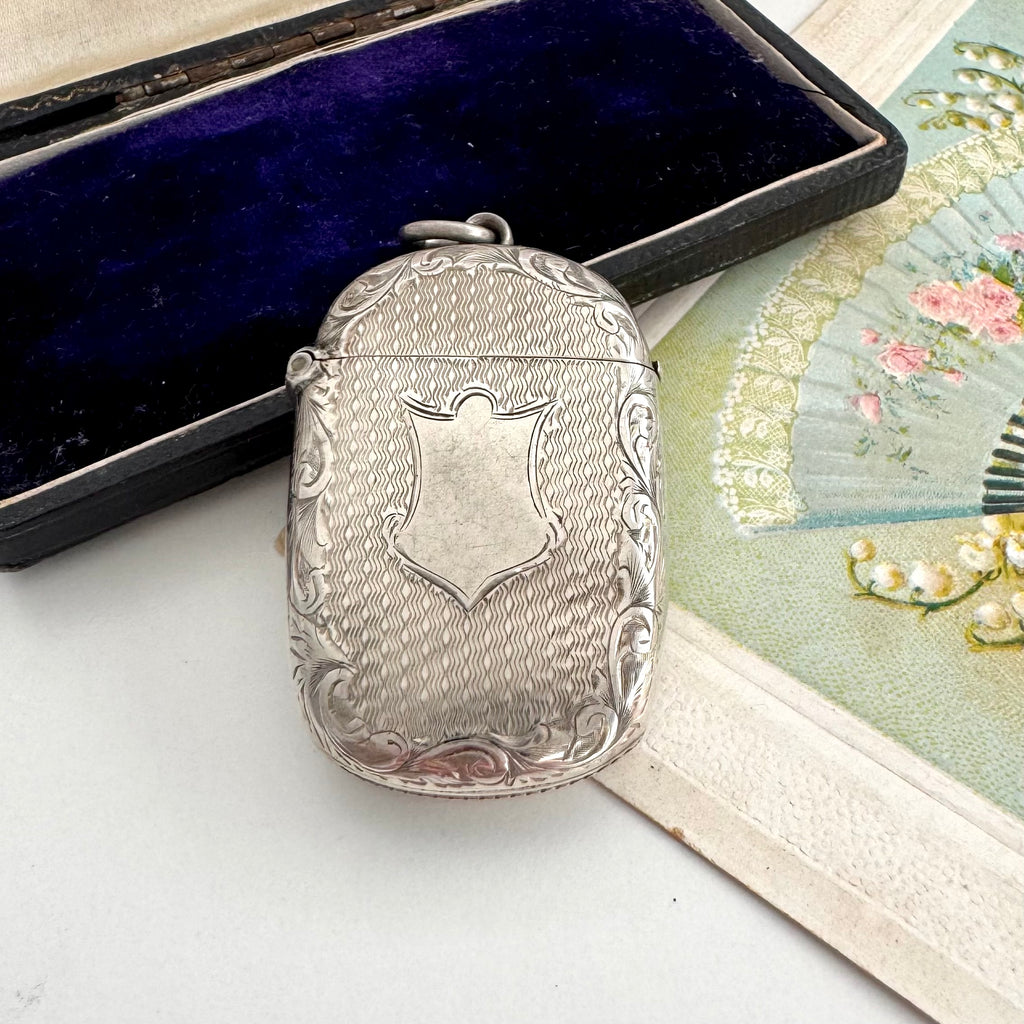 Antique 1879 Victorian silver vesta case on a white background with a vintage postcard and old box in the background.