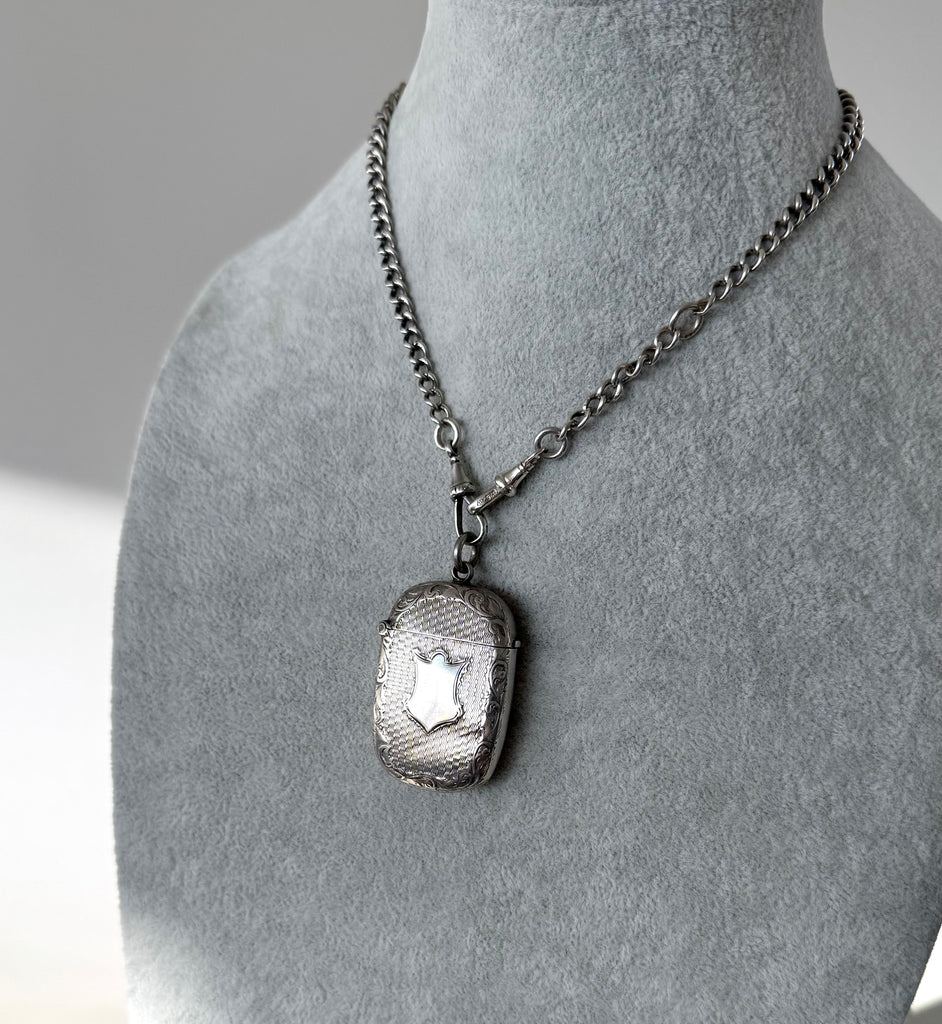 Silver antique watch chain necklace with a n antique vesta case pendant on a mannequin bust against a gray background