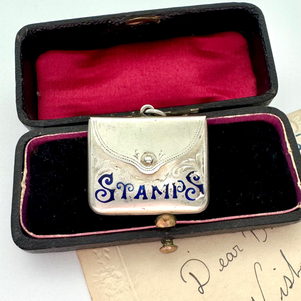 Antique 1911 Crisford & Norris silver stamp case with 'STAMPS' in blue enamel in a black box with red interior.