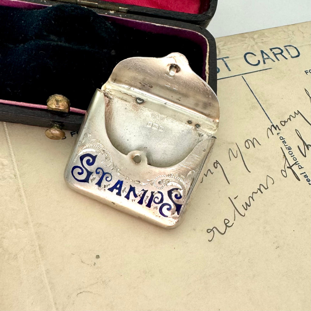 Antique 1911 Crisford & Norris silver stamp case with 'STAMPS' in blue enamel in a black box with red interior.