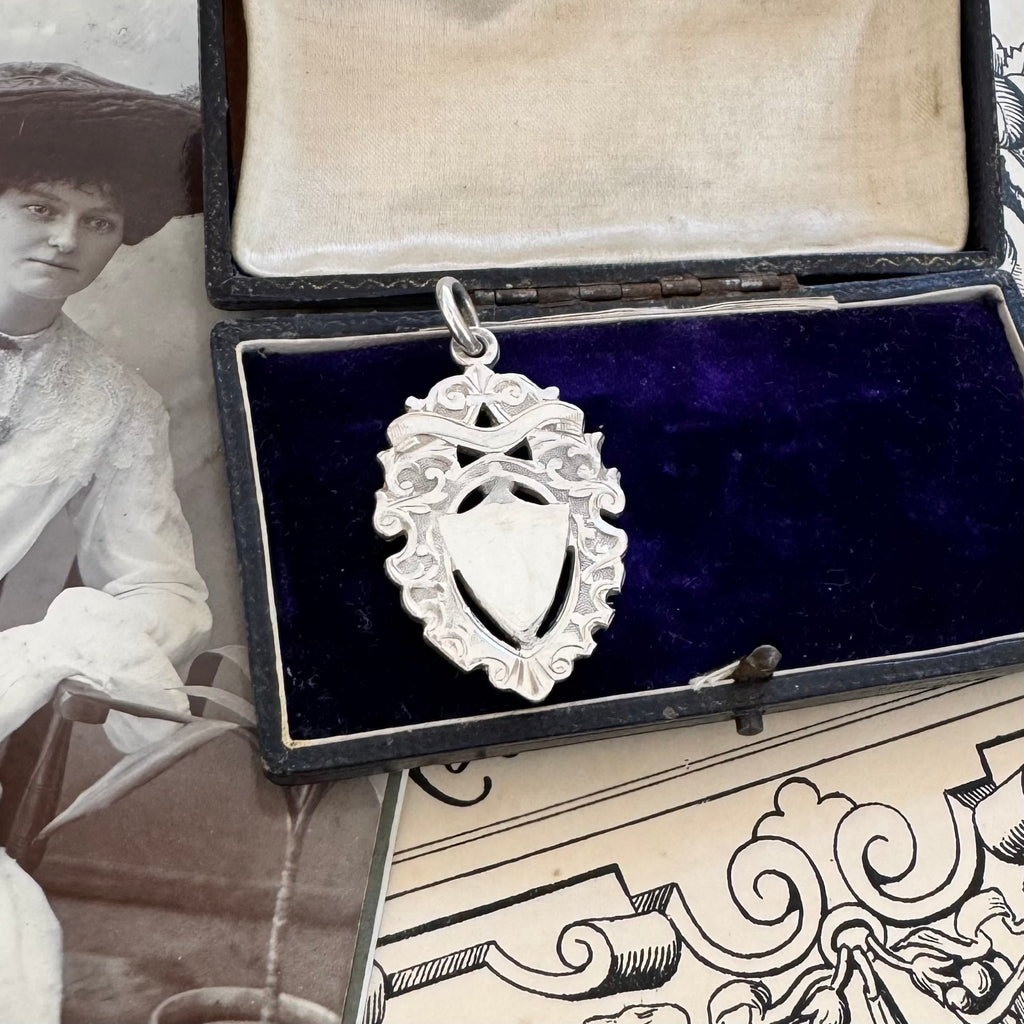 Antique silver watch fob pendant in an open jewelry box with an old photograph and decorative paper in the background