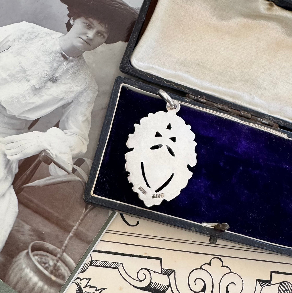 Antique silver pendant in an open jewelry box with a black and white photo of a woman in the background.