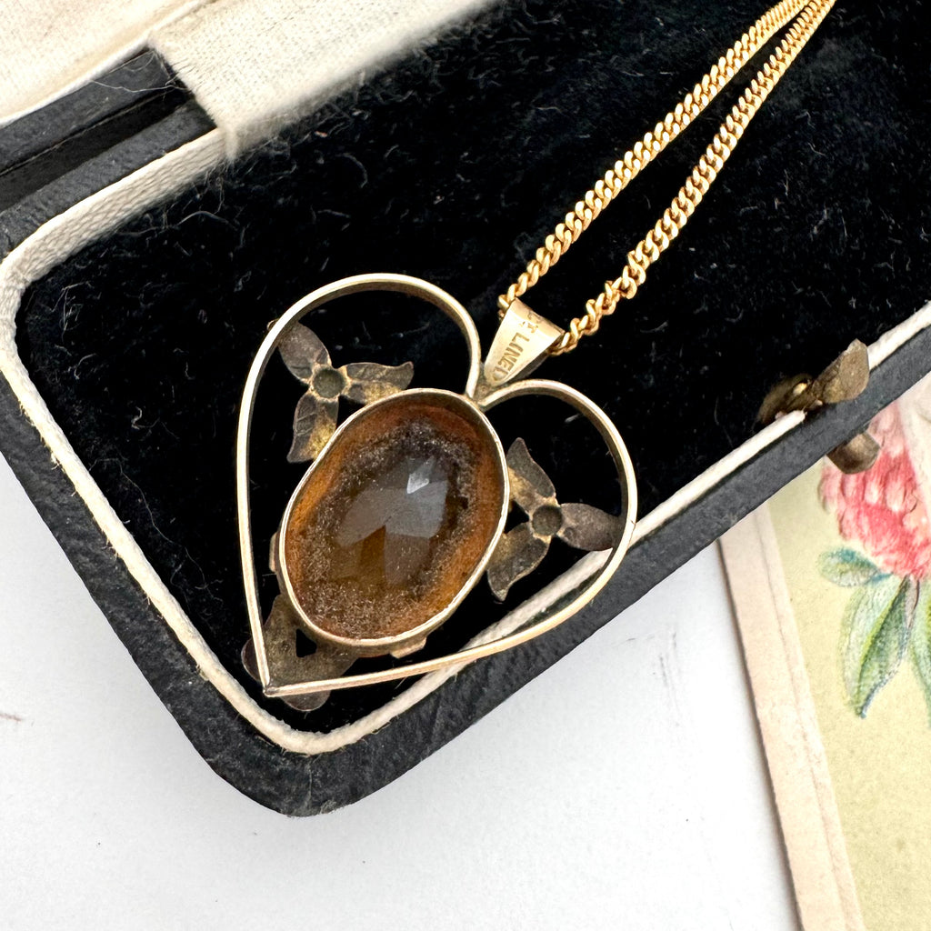 Gold necklace with a heart-shaped pendant featuring a brown stone, displayed in a black jewelry box.
