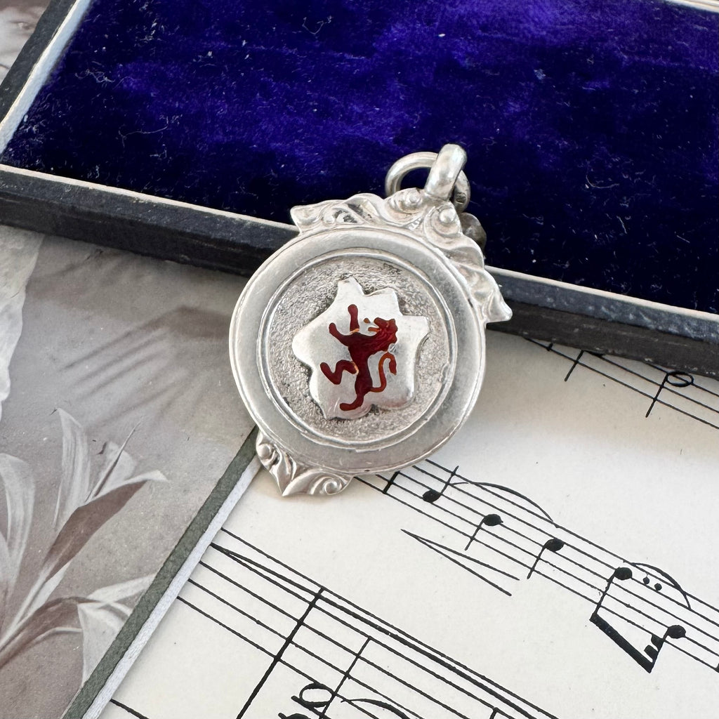 Antique silver and red enamel Lion Rampant watch fob pendant on a sheet of music