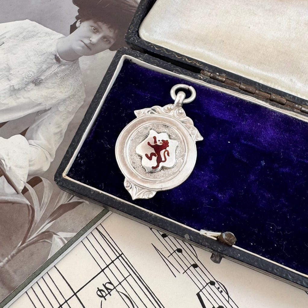 Antique silver and red enamel Lion Rampant watch fob pendant on a sheet of music