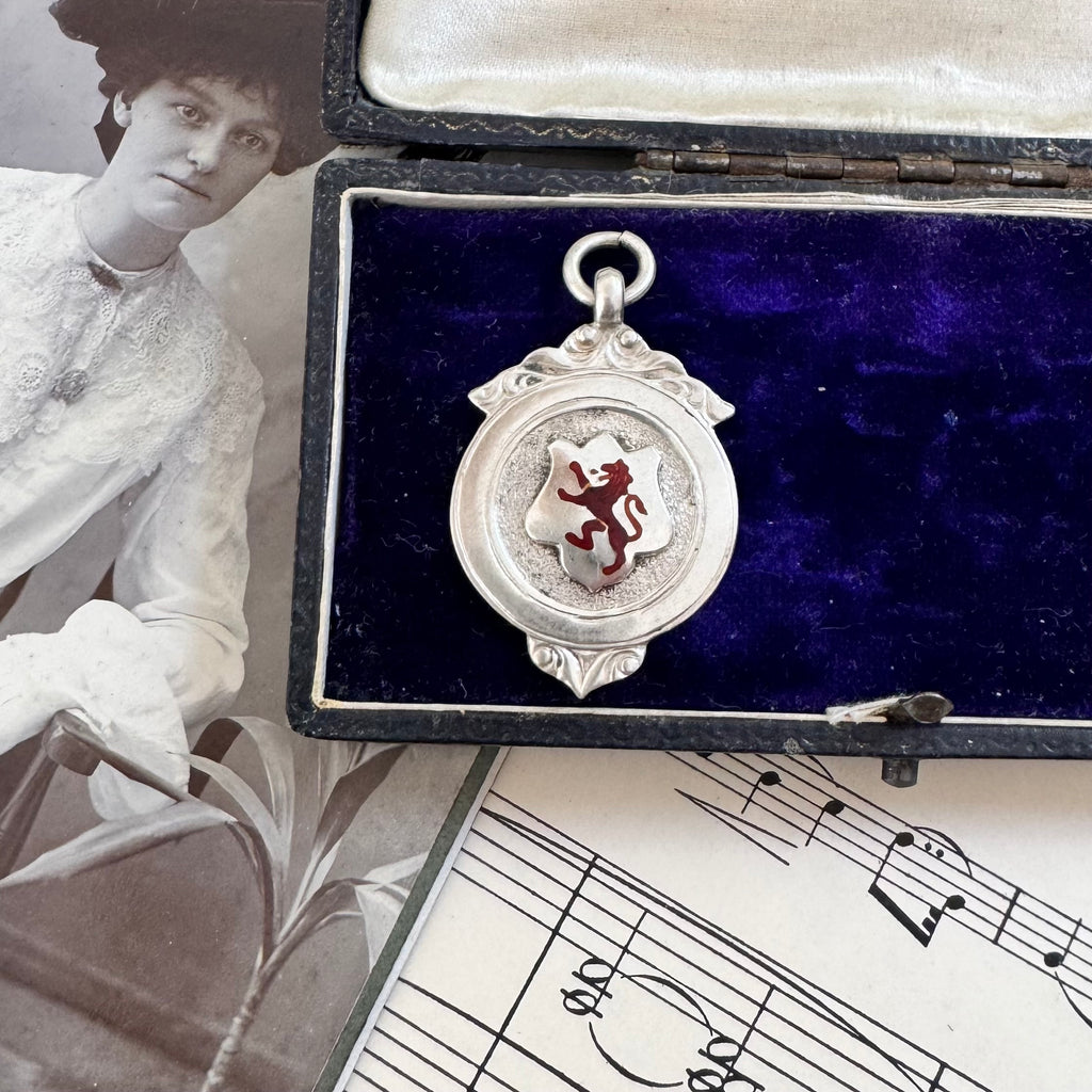 Antique silver and red enamel Lion Rampant watch fob pendant on a sheet of music