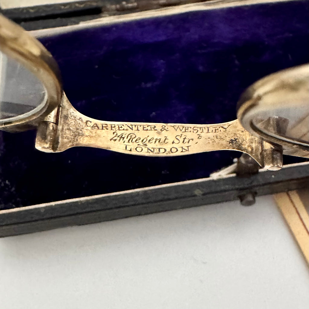 Vintage eyeglasses with 'Carpenter & Westley' engraving on a purple cushioned base.
