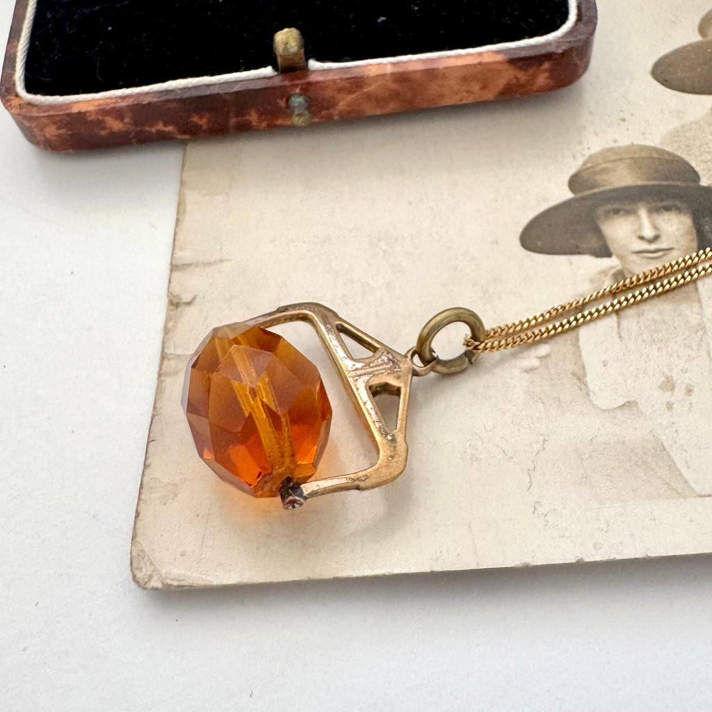 An antique Victorian paste citrine spinning fob necklace, displayed on a vintage-style printed card next to a wooden jewelry box.