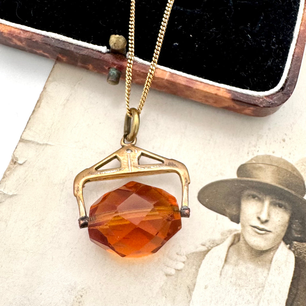An antique Victorian paste citrine spinning fob necklace, displayed on a vintage-style printed card next to a wooden jewelry box.