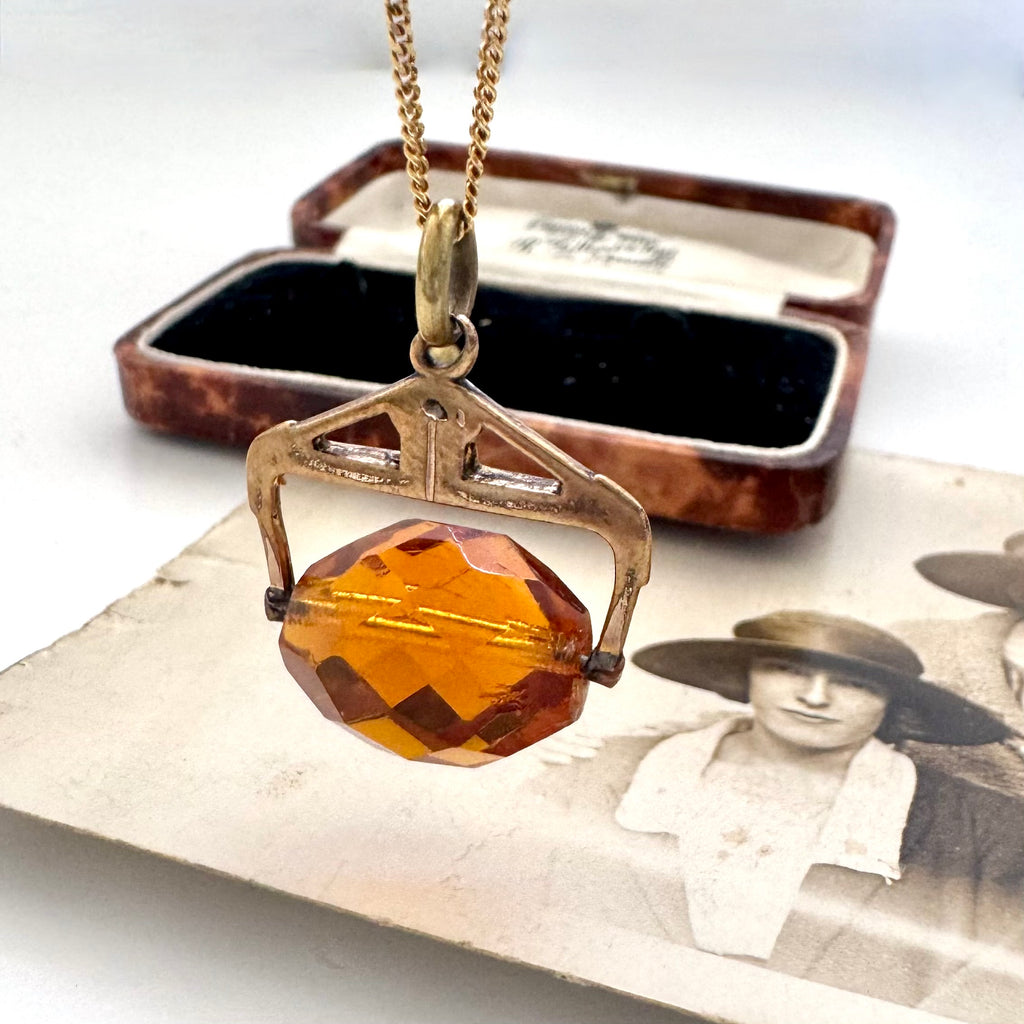 An antique Victorian paste citrine spinning fob necklace, displayed on a vintage-style printed card next to a wooden jewelry box.