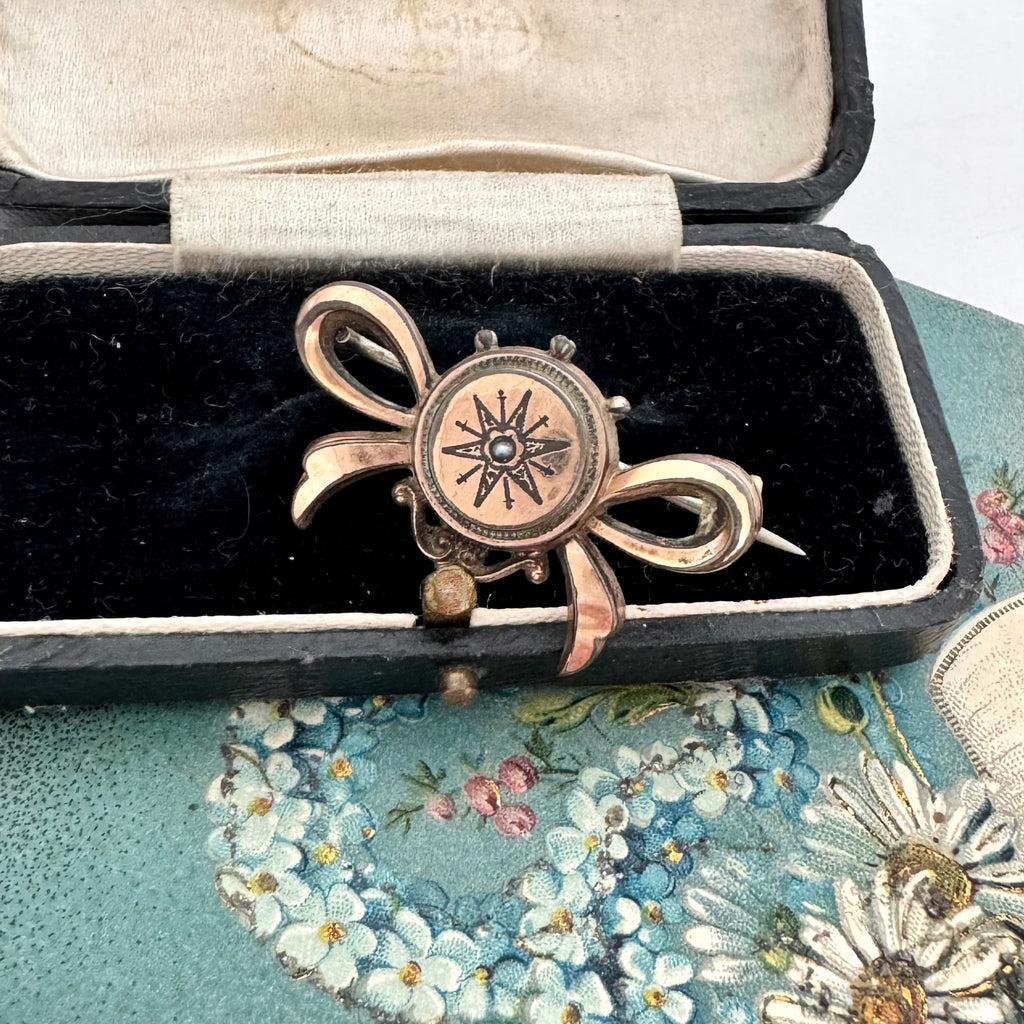 Antique Victorian star burst and bow-shaped brooch displayed on a vintage jewellery box and with a floral card in the background.