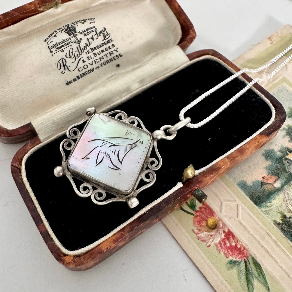 A silver pendant necklace with an iridescent mother-of-pearl square pendant and a white chain, displayed inside an open vintage wooden presentation box with black velvet lining. The inside lid shows the brand name 'R.