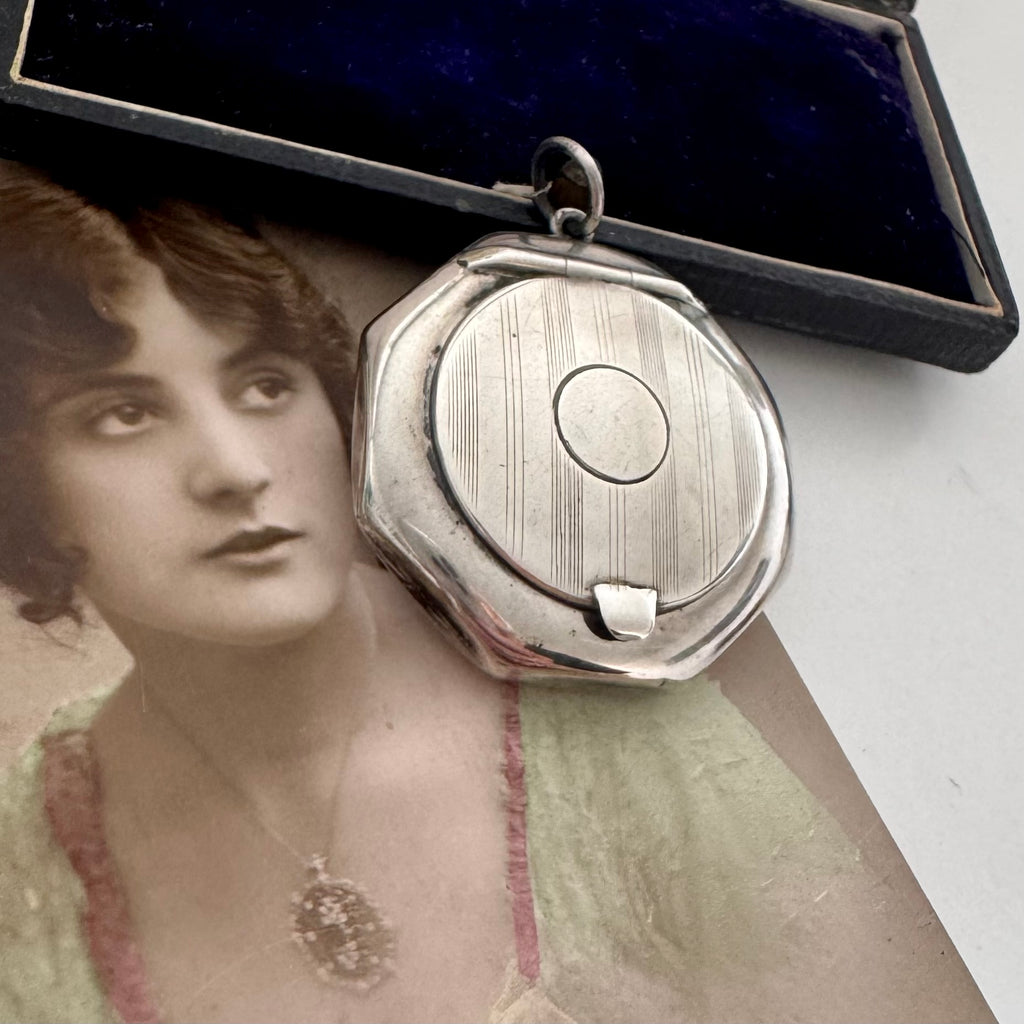 Antique silver compact locket on a white surface with an old photograph of a woman in the background.