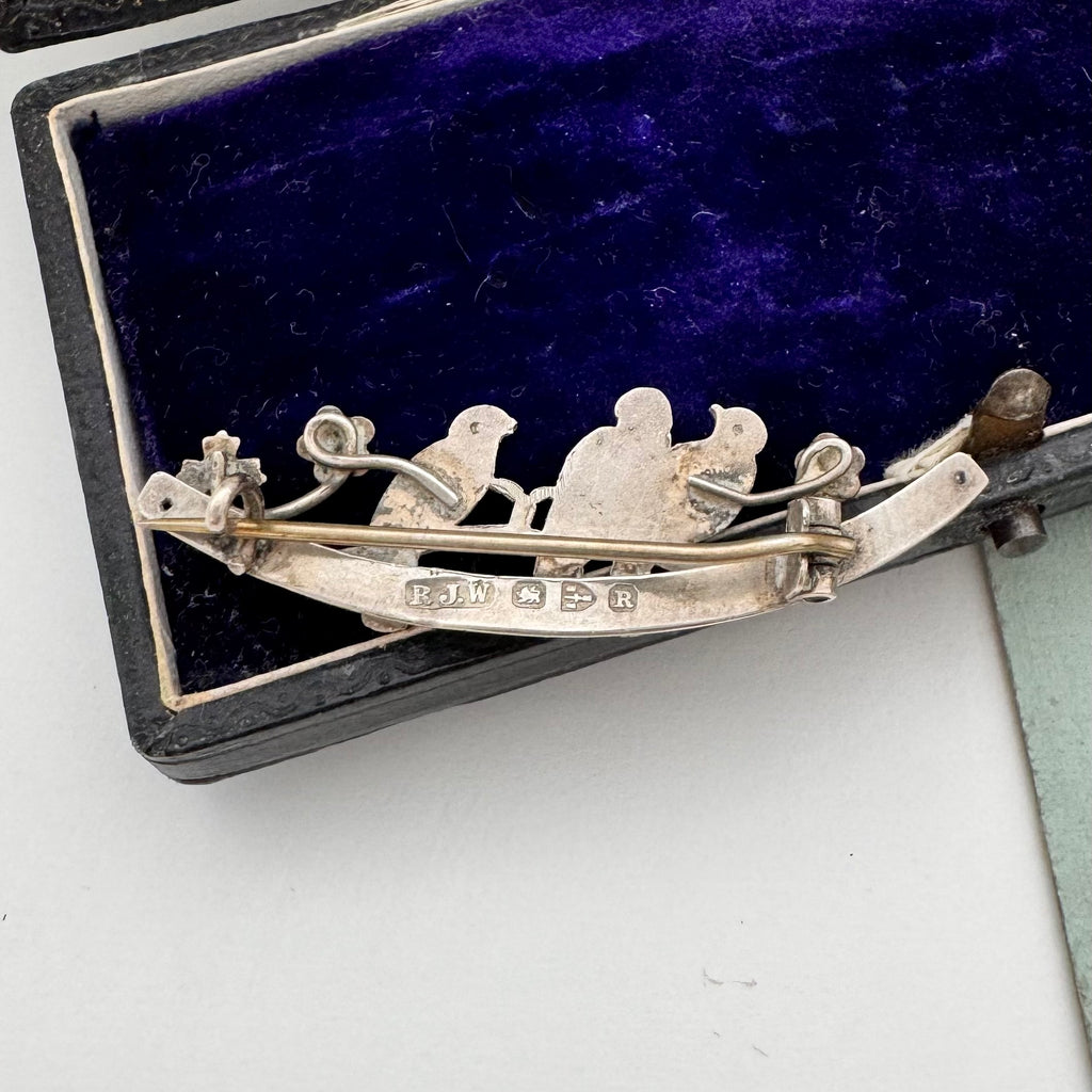 Silver brooch with three birds on a branch on a white background