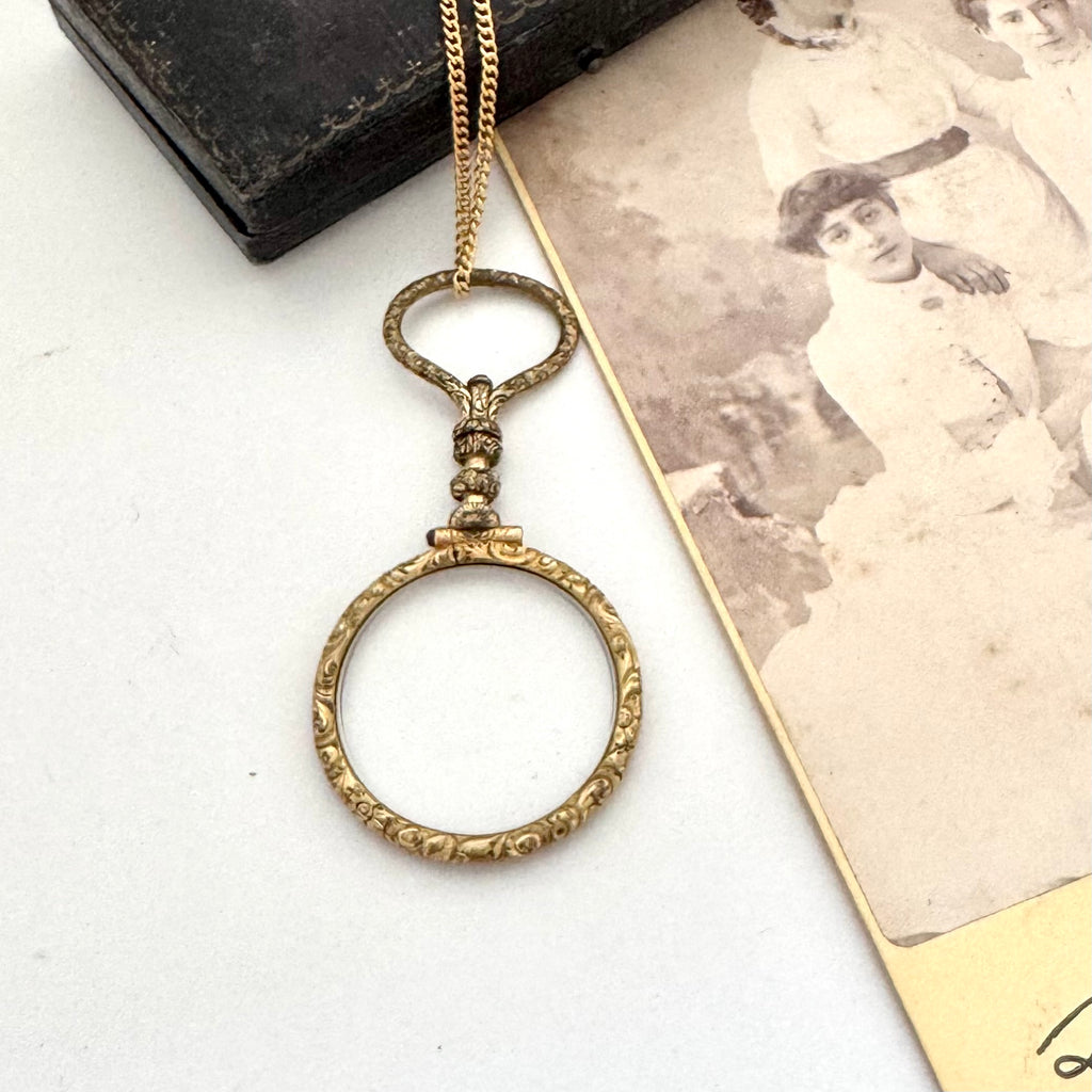 Antique gold fill magnifying glass necklace on a white surface with an old photograph.