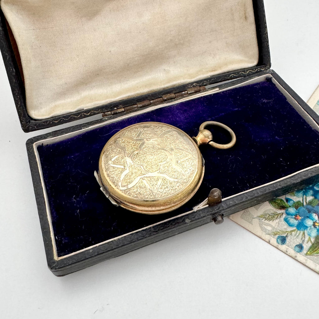 Antique pocket watch style locket with intricate design in an open jewelry box.