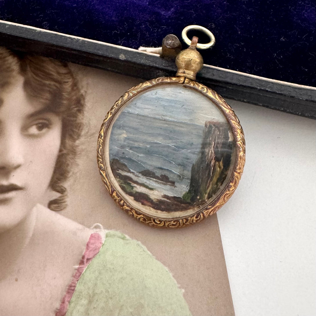 Antique rolled gold pendant with scenic design on a surface next to an old photograph