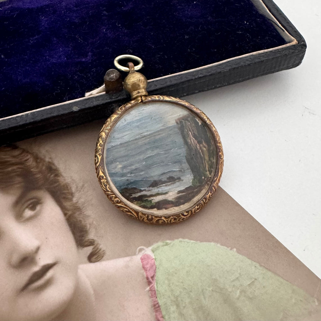 Antique rolled gold pendant with scenic design on a surface with an old photograph