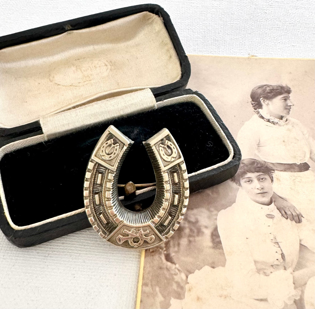 Antique horseshoe brooch in an open black box with an old photograph of a woman in the background