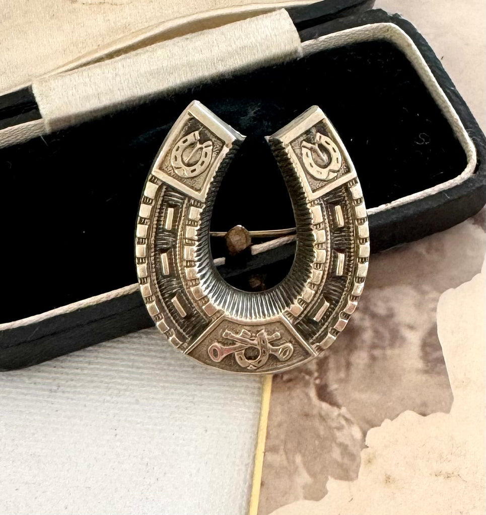 Decorative Victorian horseshoe brooch with intricate designs on a textured surface