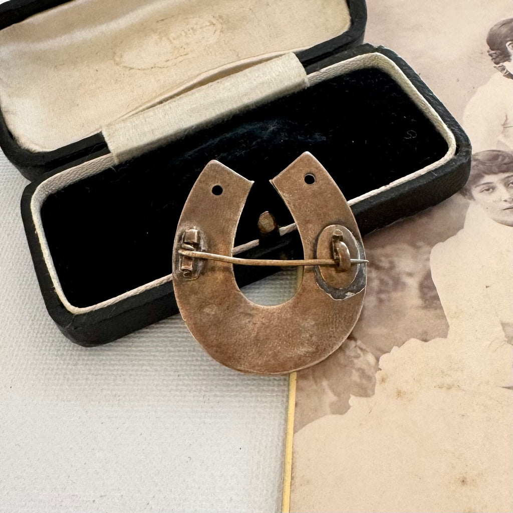 Back of antique horseshoe brooch in an open jewelry box with an old photograph in the background