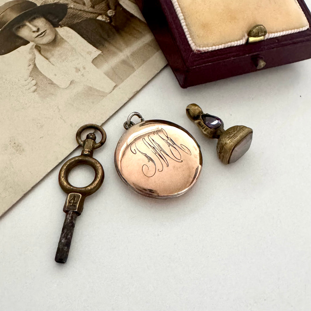 Vintage key and locket with initials on a white surface next to an old photograph.