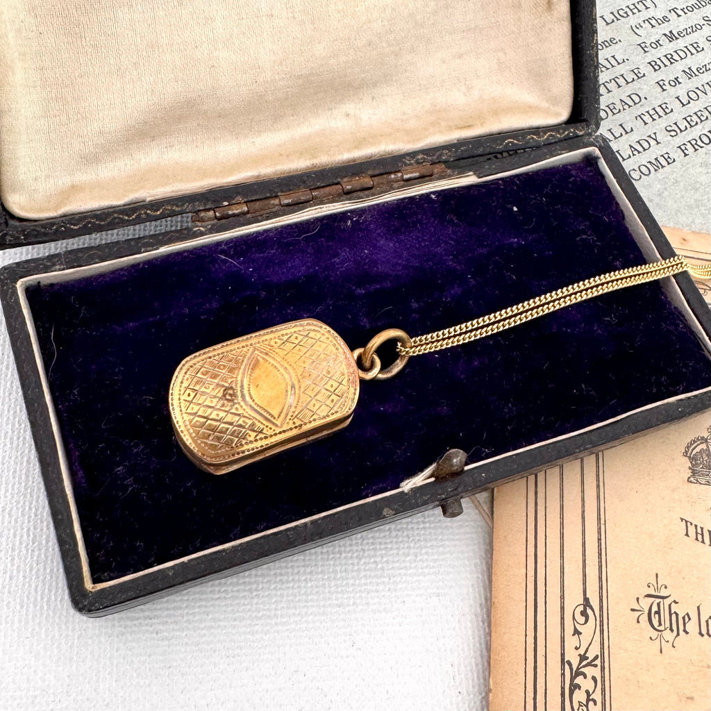 Antique pinchbeck vinaigrette on a chain with an old document in the background and on an open jewellery box