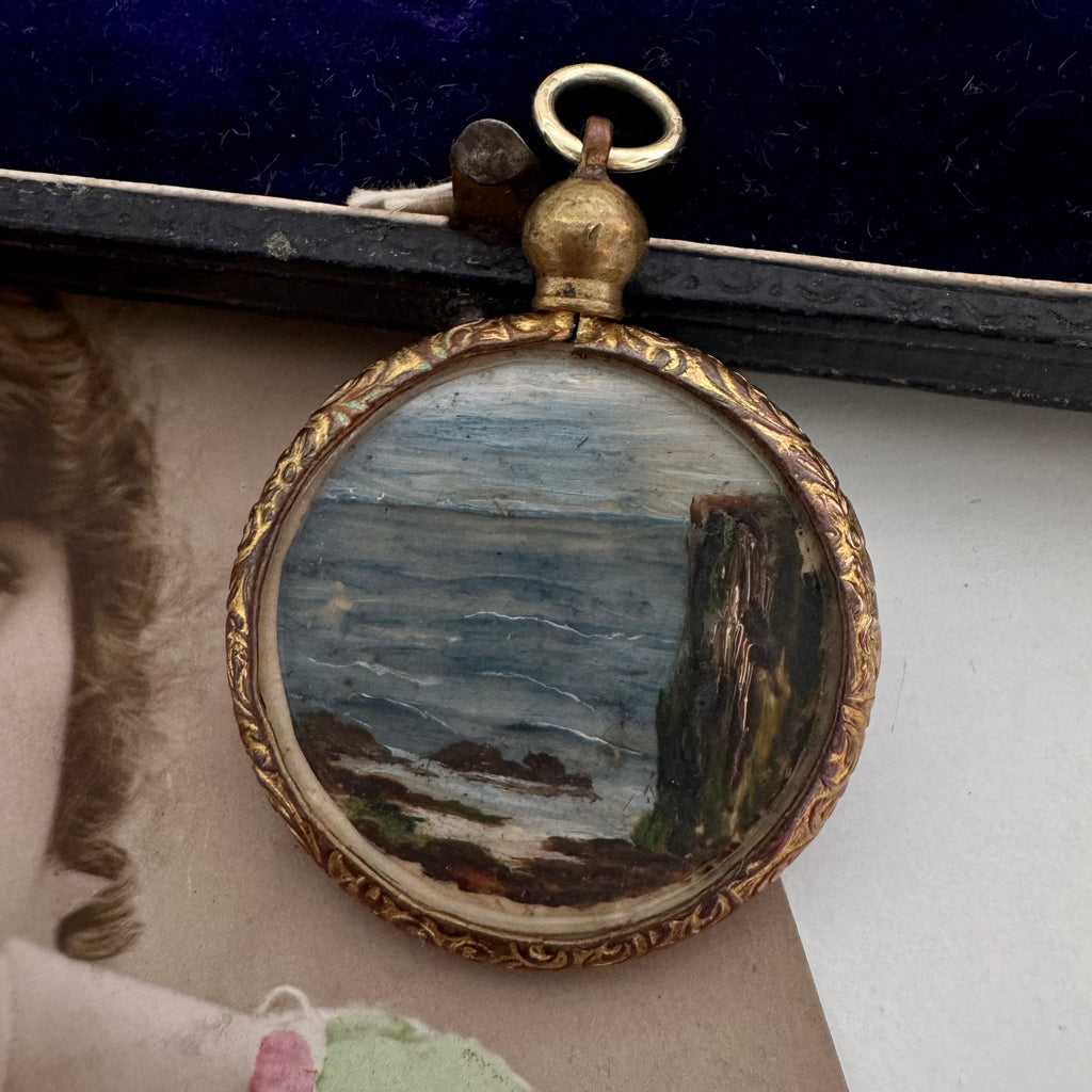 Small round painting of a landscape with a gold frame, attached to a larger portrait.