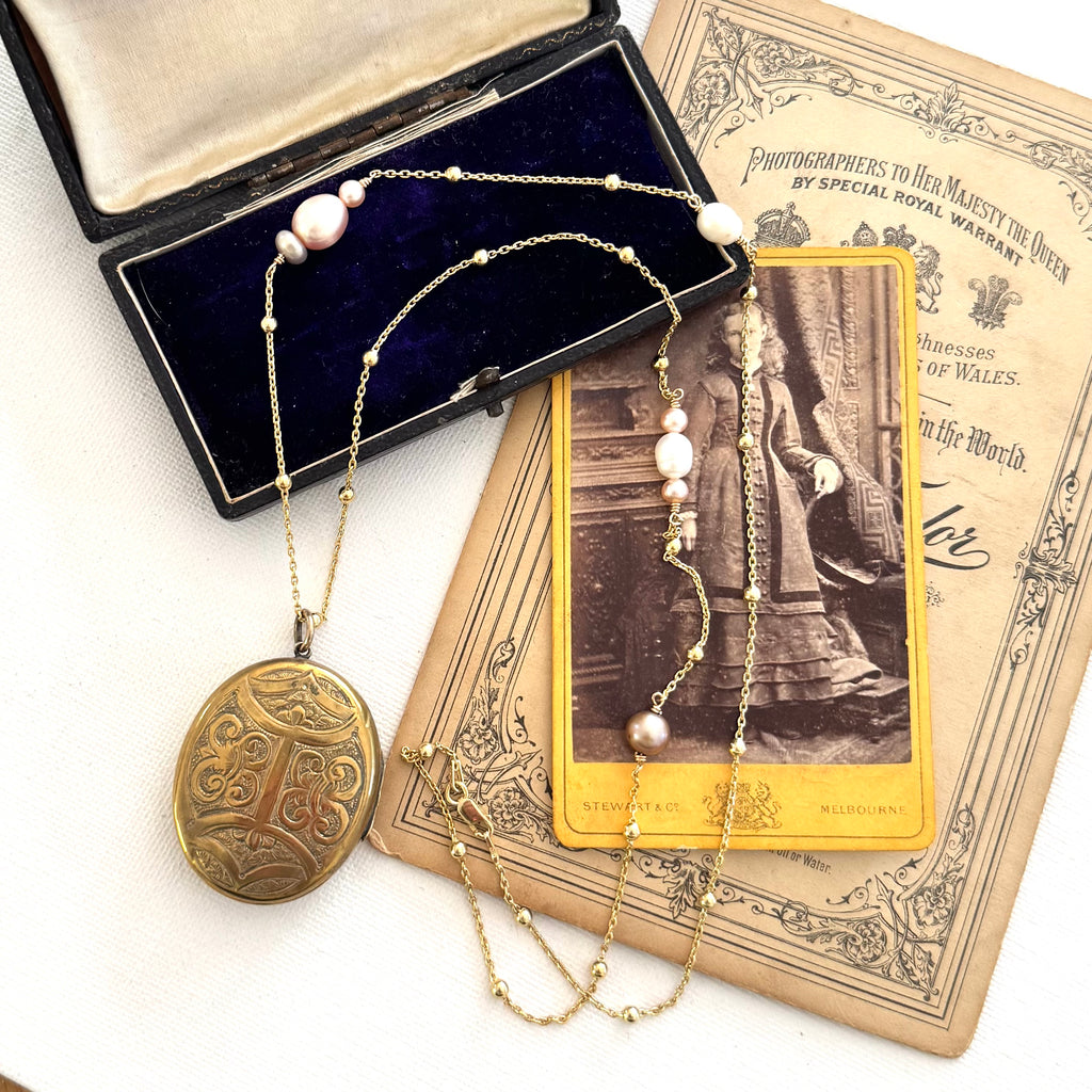 Antique locket on a gold and pearl chain on old photos and jewellery box