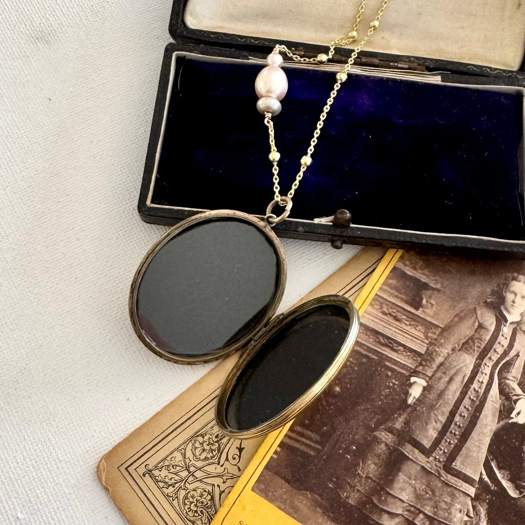 Antique locket on a gold and pearl chain on old photos and jewellery box