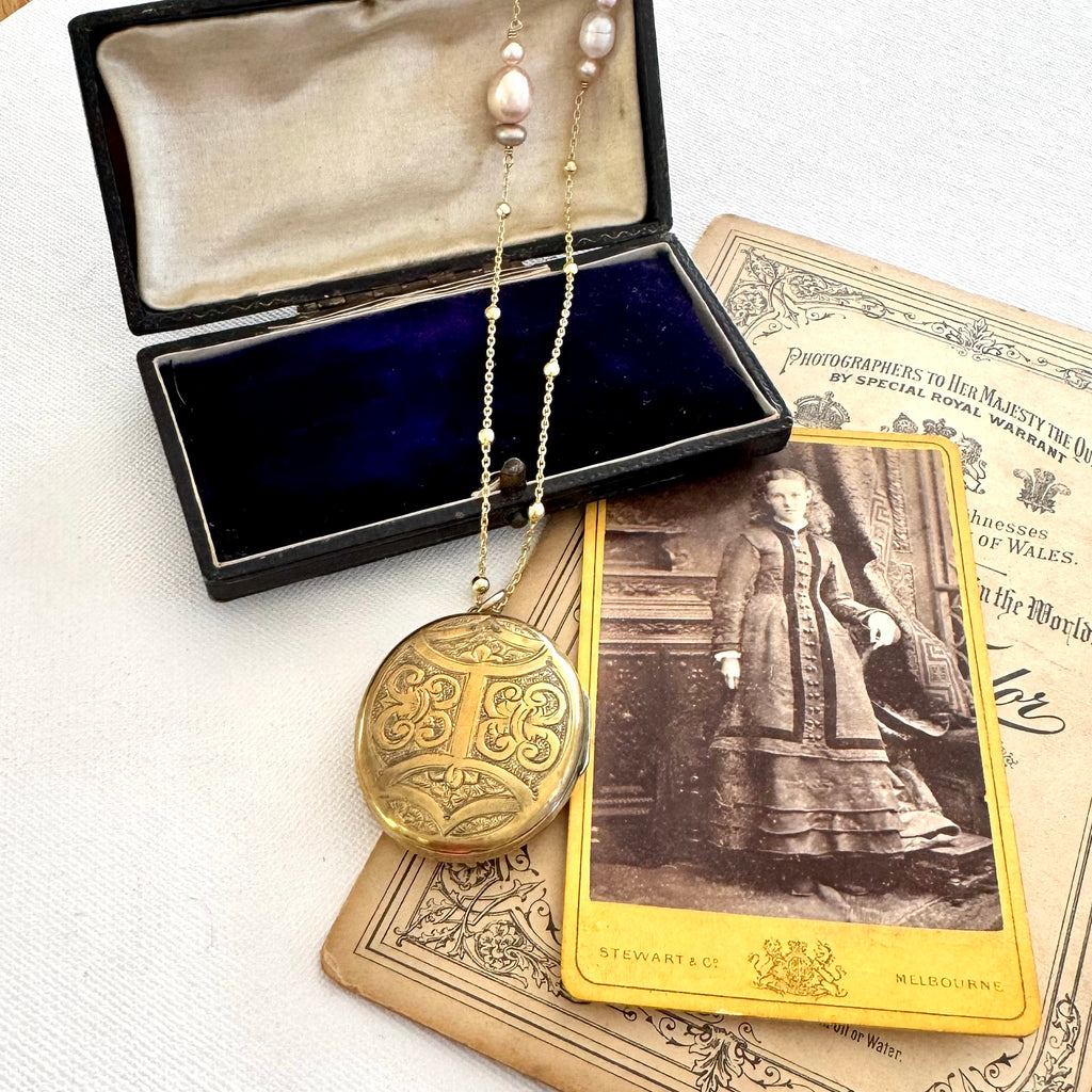 Antique locket on a gold and pearl chain on old photos and jewellery box