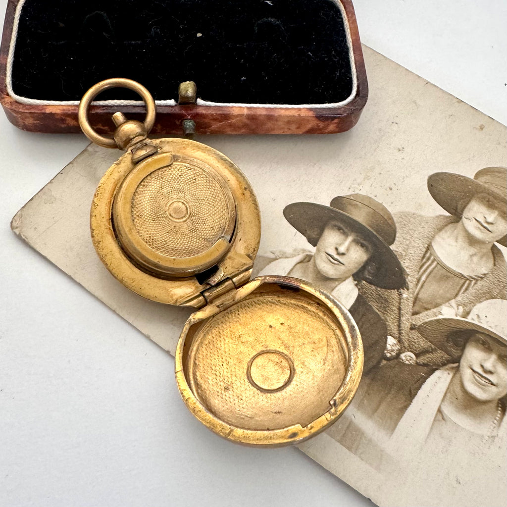 An antique gold-toned sovereign case is shown open, resting on top of an old sepia photograph. A rectangular wooden keepsake box with a black velvet interior is visible in the upper left against a plain light background.