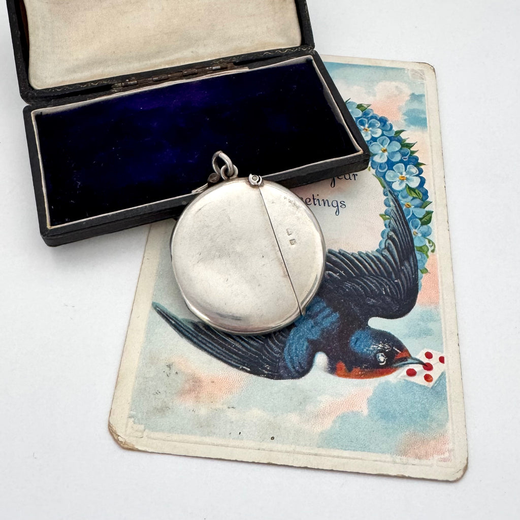 Antique silver round vesta case with a bird design on a vintage card